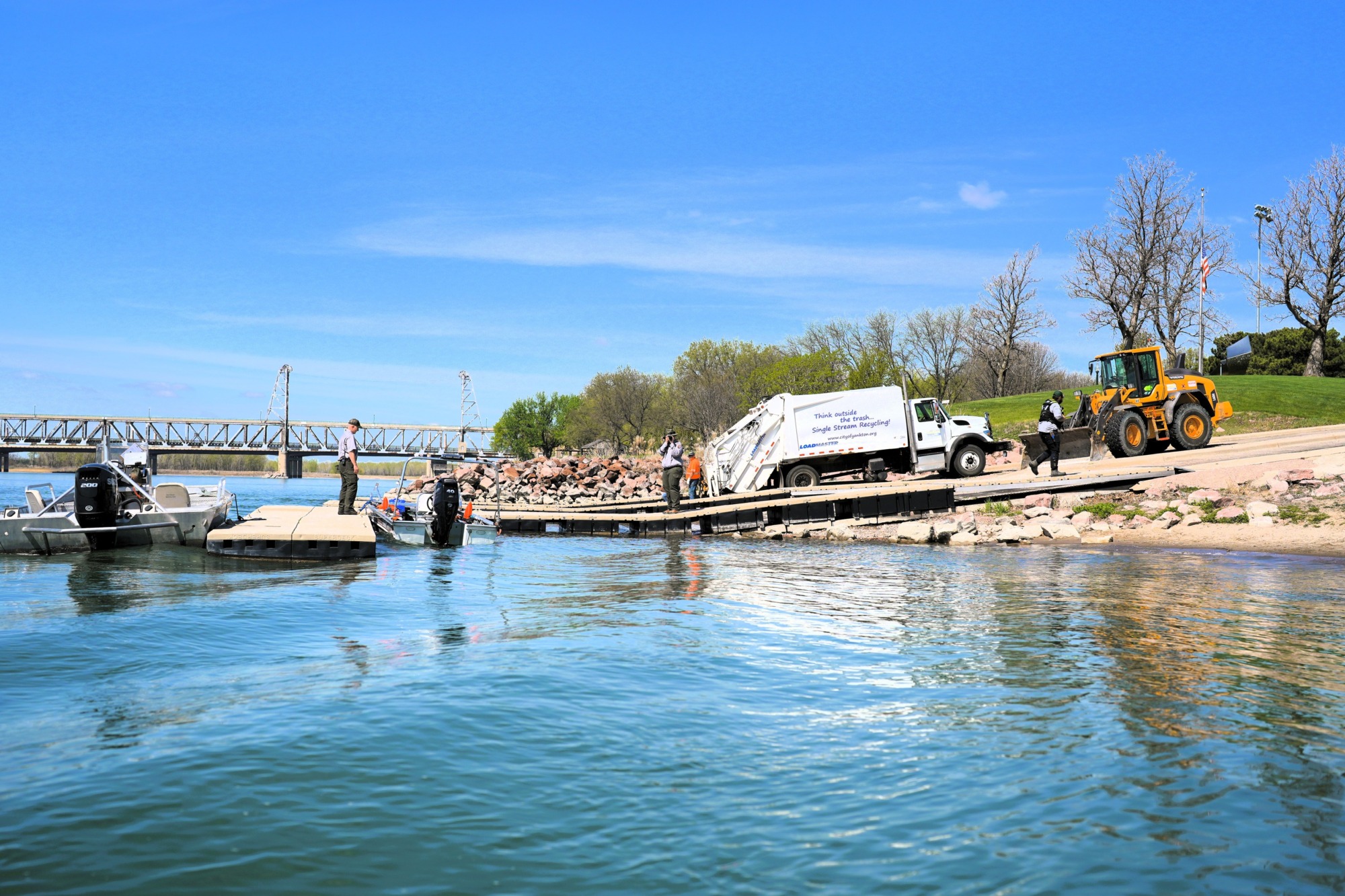 A view of a boat ramp with a multiple boats docked and a garbage truck parked on the ramp.