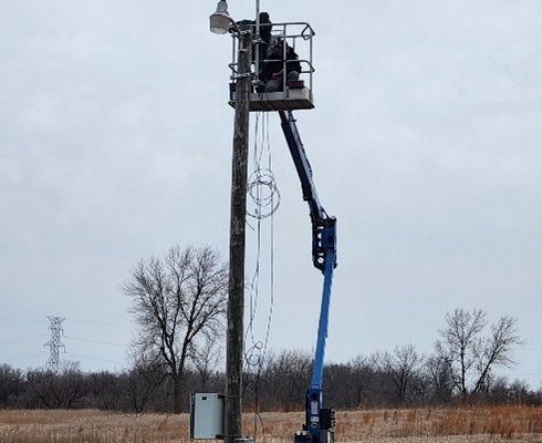 A tall metal tower with antennas across it gets installed in an open field