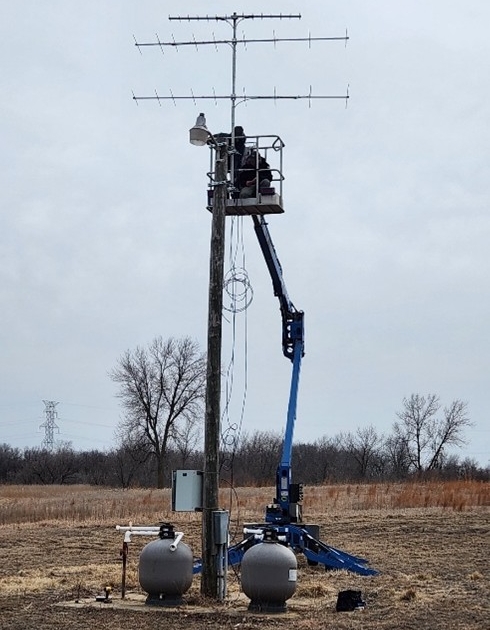 A tall metal tower with antennas across it gets installed in an open field