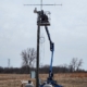A tall metal tower with antennas across it gets installed in an open field