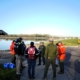 A group of people circle up near a life jacket loaner station and boat ramp
