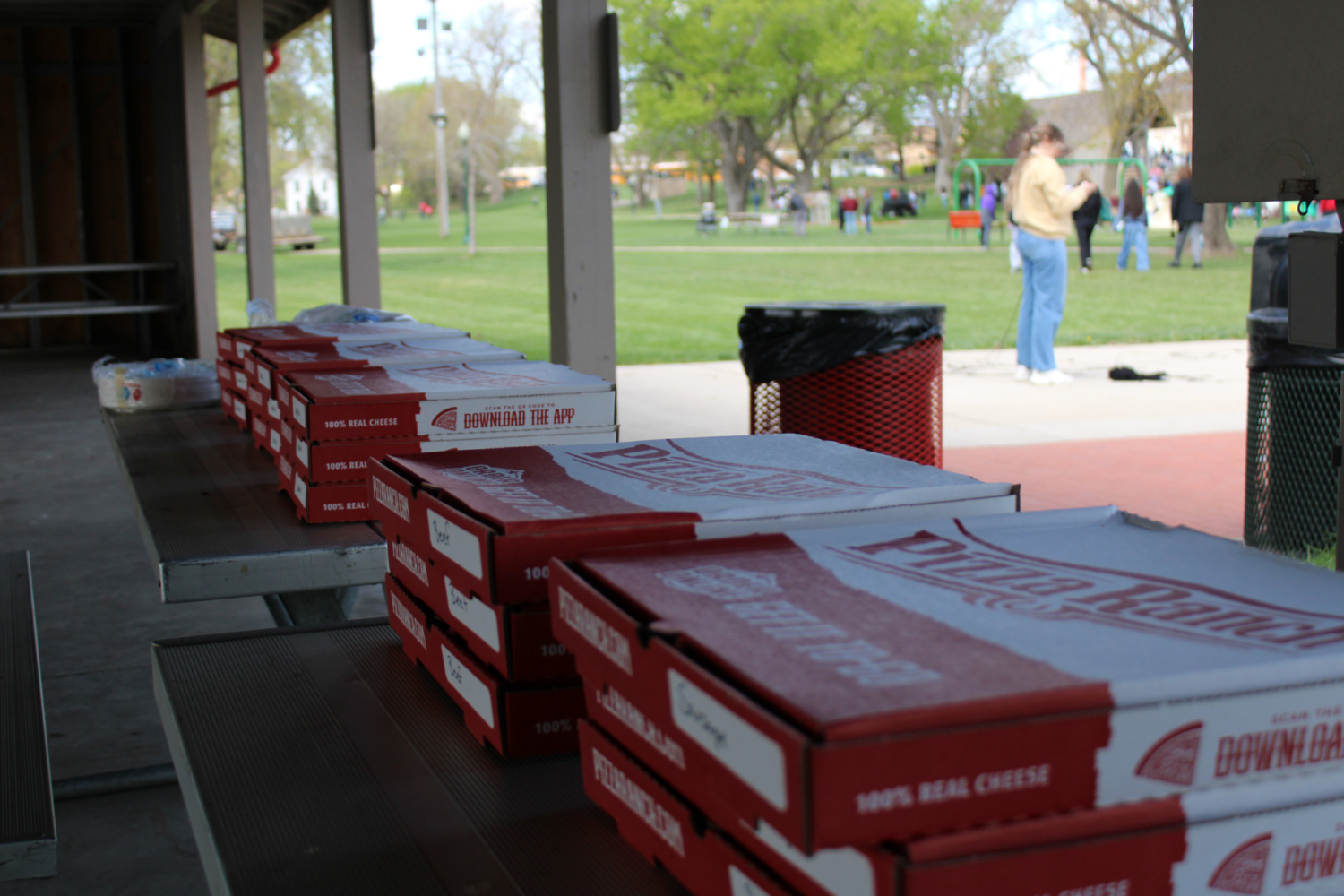 Pizza boxes lay lined up on a picnic table.