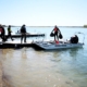 people walk along a dock as one person carries two trash bags off a boat