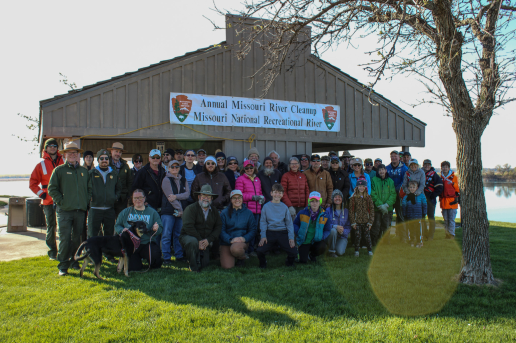 a group photo of people in front of a picnic shelter with a banner spread across is that reads, "Annual Missouri River Cleanup, Missouri National Recreational River"