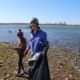 a woman smiles at the camera as she carries a trash bag, a young girl walks alongside her