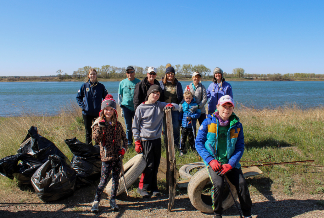 a group of people stand together for a group photo, kids in the front row pose with some trash and debris 