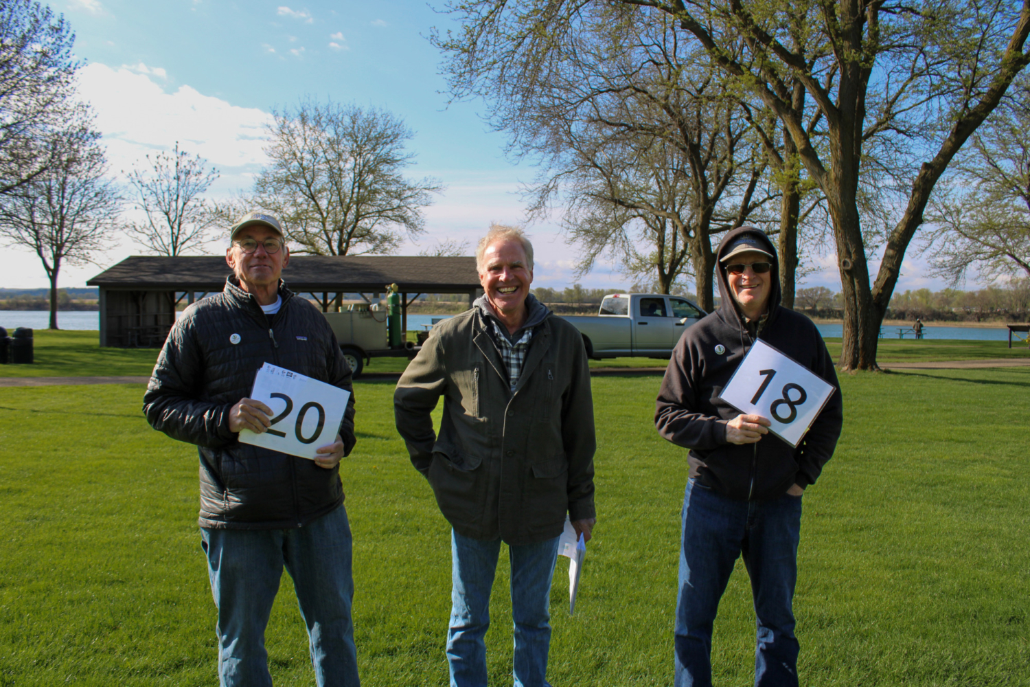 Three people stand together smiling, two hold number signs.