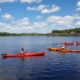 Five people paddling kayaks on the calm waters of Lake Yankton under a blue sky with white clouds