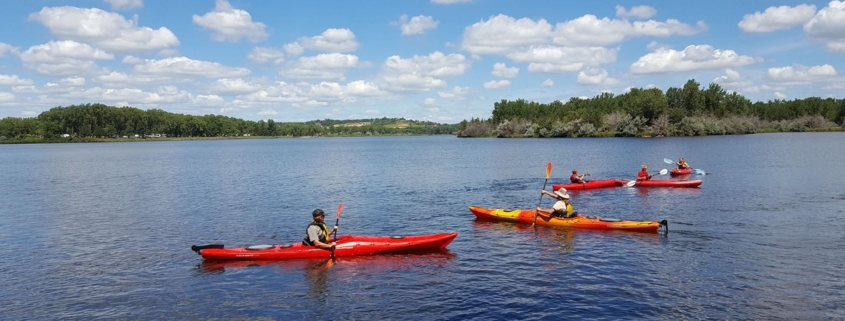 Five people paddling kayaks on the calm waters of Lake Yankton under a blue sky with white clouds