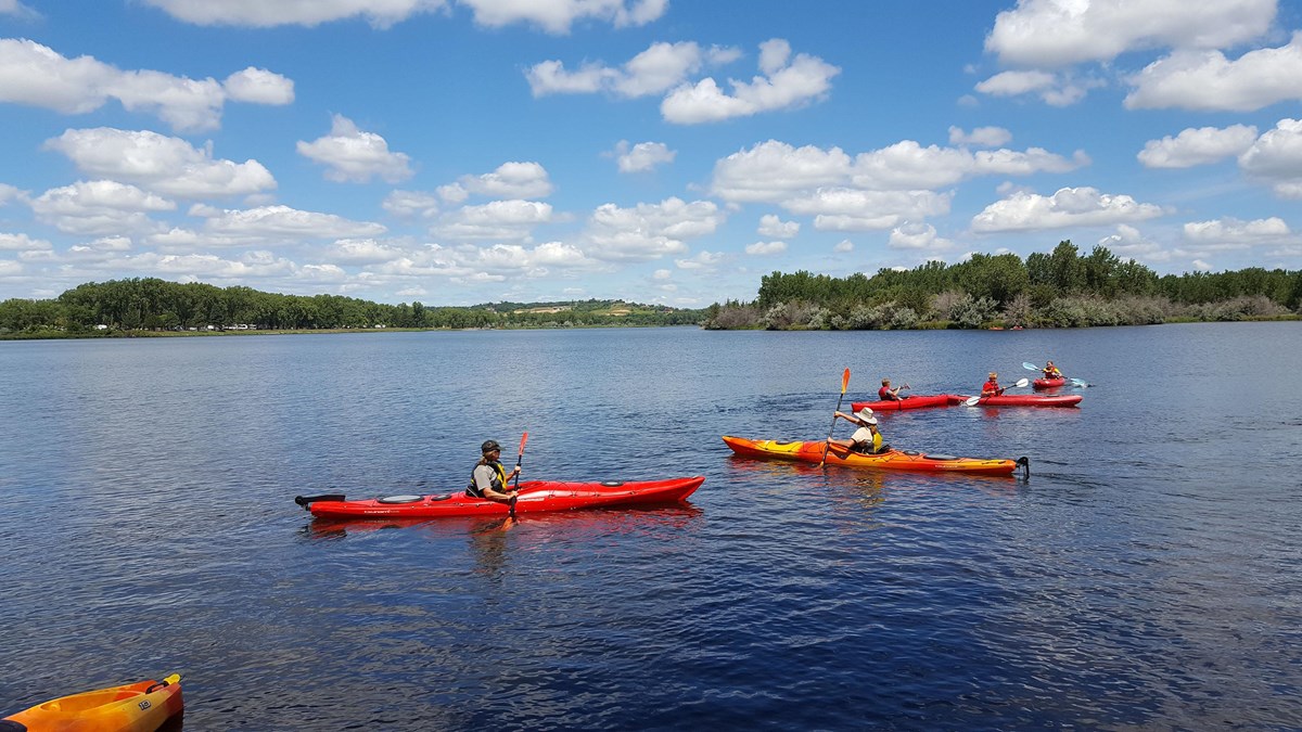 Five people paddling kayaks on the calm waters of Lake Yankton under a blue sky with white clouds